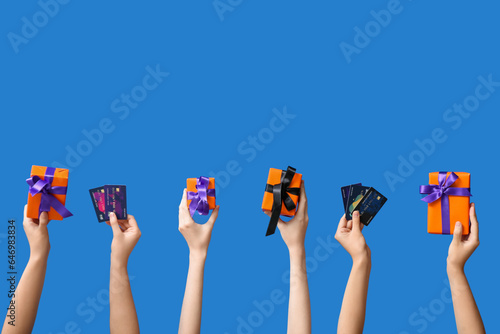 Female hands holding Halloween gifts and credit cards on blue background
