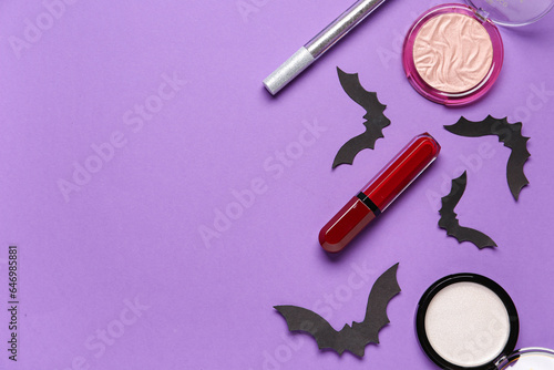 Different decorative cosmetics and paper bats for Halloween on purple background