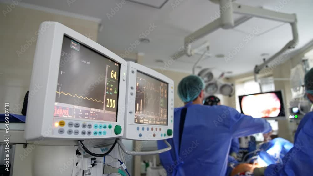 Doubled screen of a lung ventilator working in the surgery room. Medical team working in the backdrop in blur. Doubled screen of a lung ventilator working in the surgery room. Medical team working in the backdrop in blur.
