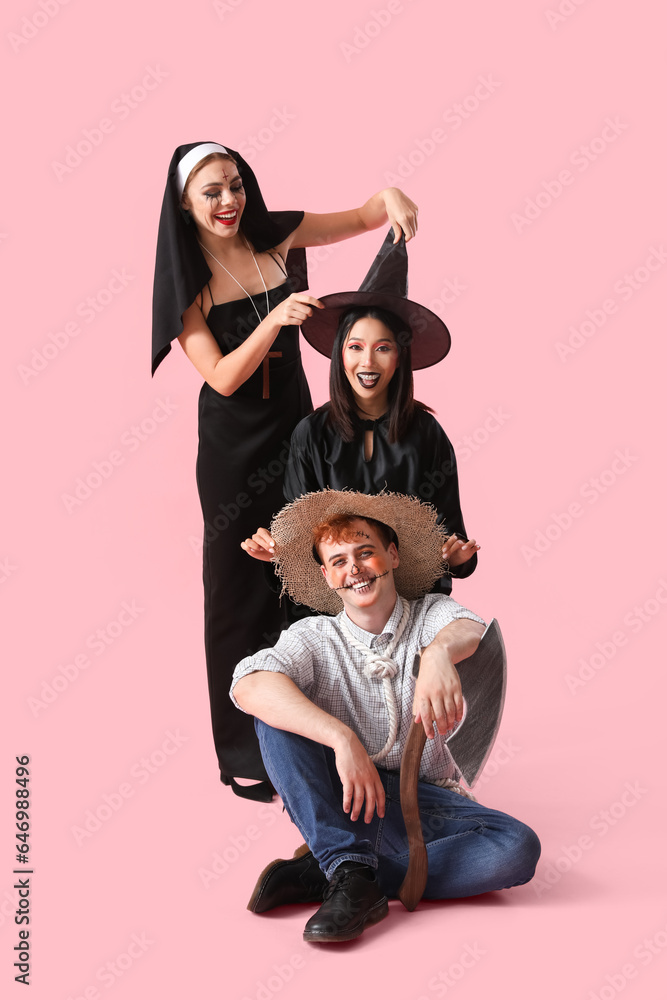 Young friends in costumes for Halloween party on pink background