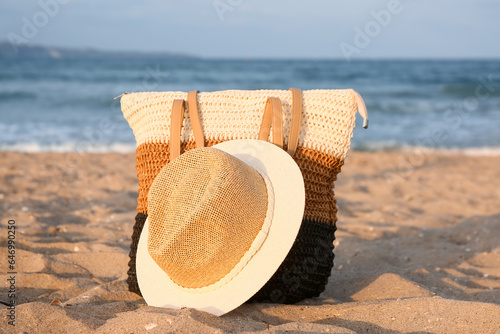 Beach bag and straw hat on sand near sea