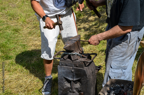 The blacksmith manually with hammer working with metal on the anvil in the open air