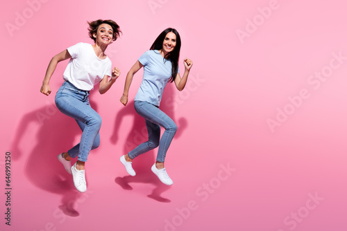 Full length body size photo of run two girls have fun energetic hurry up fast speed wear casual outfit isolated on pink color background