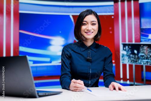 Asian presenter on daily newscast in newsroom, talking about latest international events on live broadcast. Woman reporter creating television content with media outlets headlines.