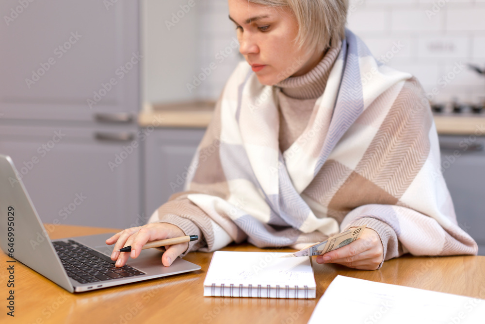 A girl in a warm cape works at home for a laptop. Girl freelancer, accountant, business woman, financier. Counts money, writes in a notebook, writes in a laptop. A girl in a warm cape works at home for a laptop. Girl freelancer, accountant, business woman, financier. Counts money, writes in a notebook, writes in a laptop.