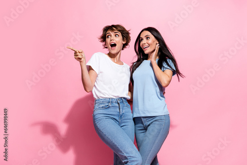 Photo of young woman two best friends unexpected pointing finger empty space new film premiere advert isolated on pink color background