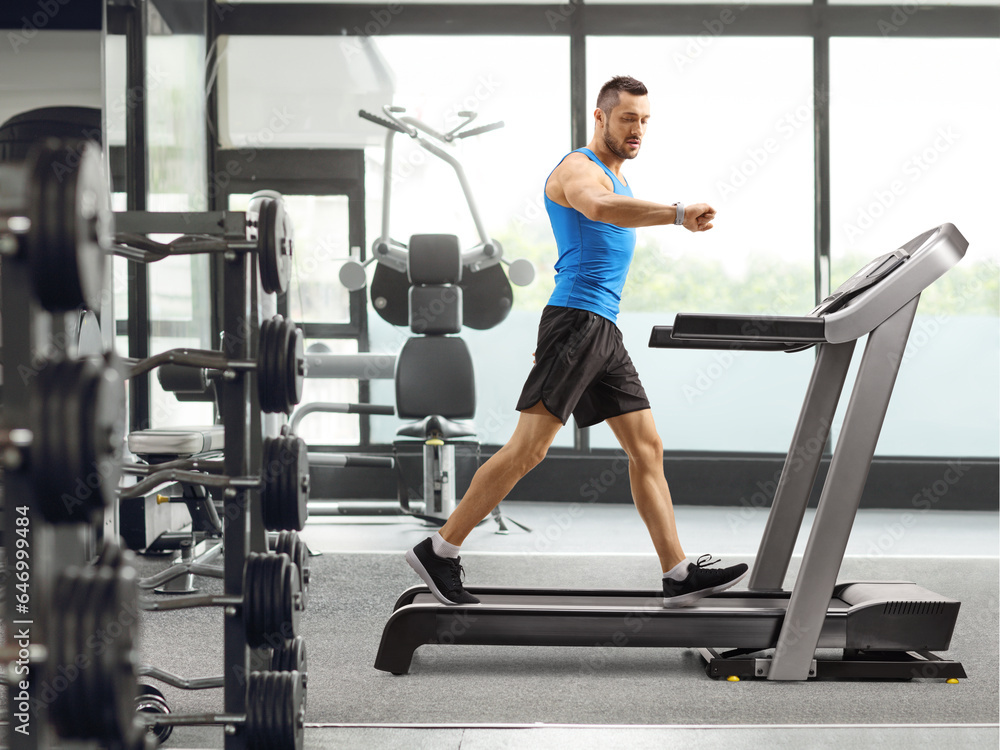 Guy exercising on a treadmill and looking at his smartwatch inside a gym Guy exercising on a treadmill and looking at his smartwatch inside a gym
