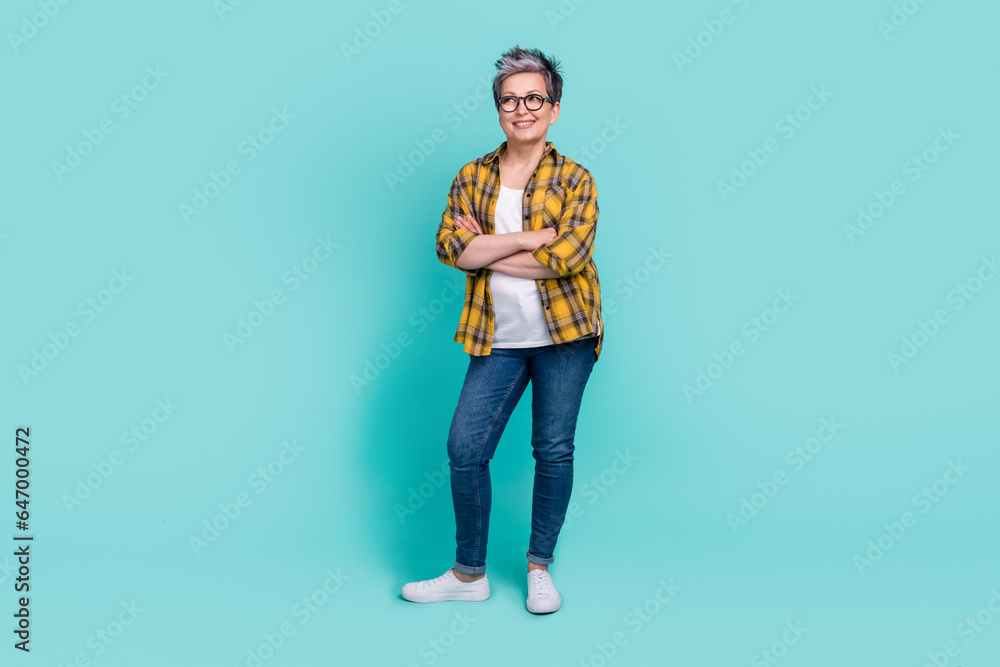 Full body size portrait of attractive grey haired senior woman holding arms folded look side isolated aquamarine color background Full body size portrait of attractive grey haired senior woman holding arms folded look side isolated aquamarine color background