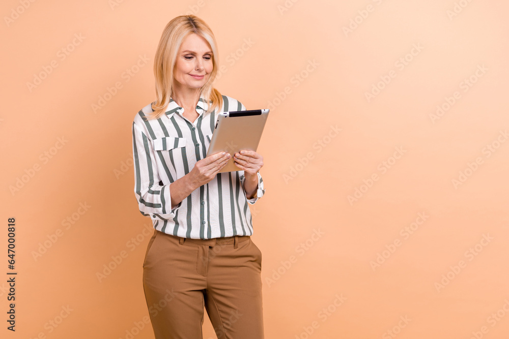 Photo of cheerful serious senior woman with bob hairstyle striped shirt look at tablet read email isolated on pastel color background Photo of cheerful serious senior woman with bob hairstyle striped shirt look at tablet read email isolated on pastel color background