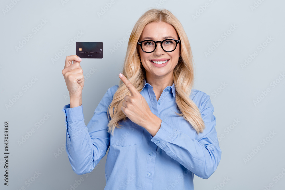 Portrait of cheerful young business worker lady blonde curls direct finger plastic credit payment card isolated on grey color background
