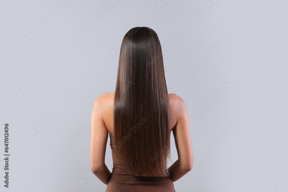 Hair styling. Woman with straight long hair on grey background, back view Hair styling. Woman with straight long hair on grey background, back view