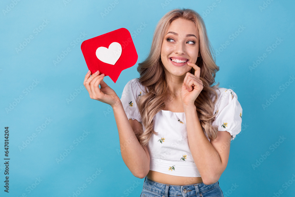Portrait of young girlfriend bite finger hold heart figure symbol looking dreamy admiring affection heart isolated on blue color background Portrait of young girlfriend bite finger hold heart figure symbol looking dreamy admiring affection heart isolated on blue color background