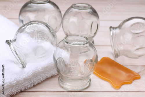 Glass cups, towel and gua sha on white wooden table, closeup. Cupping therapy photo