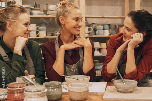 A company of three cheerful young women friends are painting ceramics in a pottery workshop.