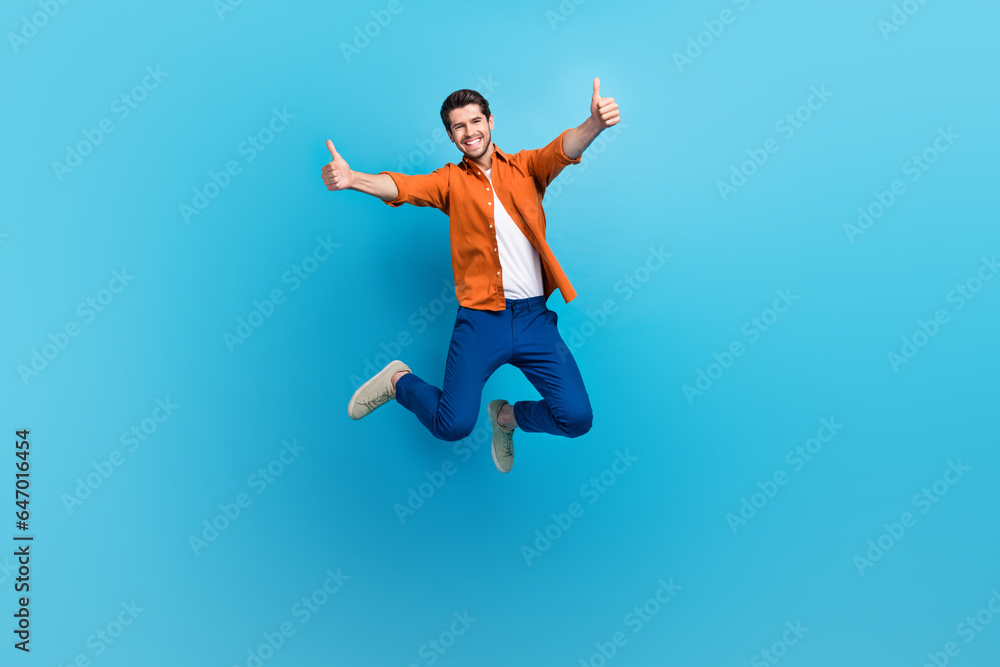 Full size photo of attractive overjoyed crazy person jumping hands fingers demonstrate thumb up approval isolated on blue color background Full size photo of attractive overjoyed crazy person jumping hands fingers demonstrate thumb up approval isolated on blue color background