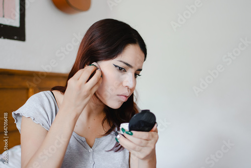 Joven mujer de piel clara con cabello rojizo utilizando un espejo de mano para maquillarse photo