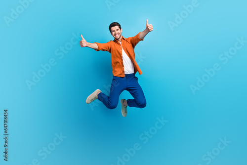 Full size photo of attractive overjoyed crazy person jumping hands fingers demonstrate thumb up approval isolated on blue color background