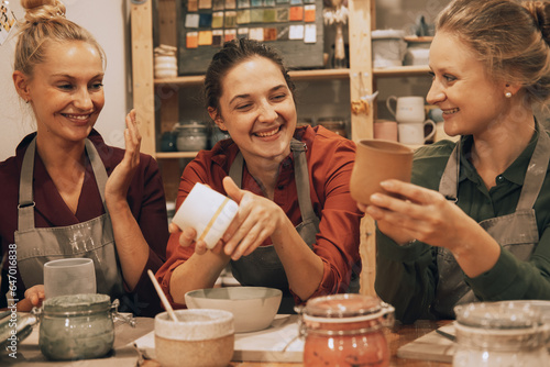 A company of three pretty young women friends make ceramic mugs in a pottery workshop.