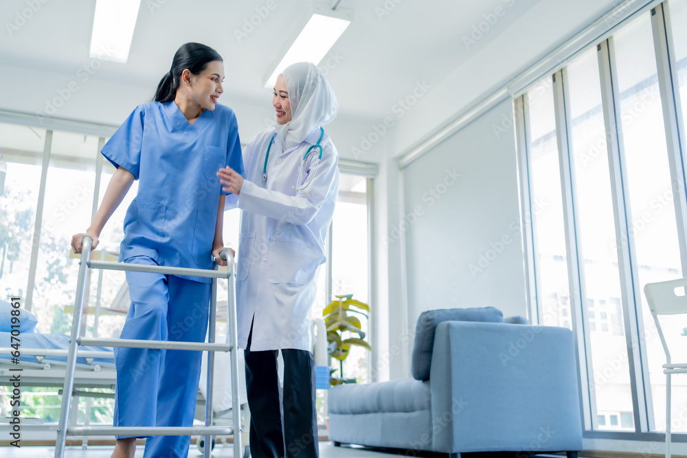A Muslim Female doctor help a patient who is doing physical therapy and is practicing walking with a walking stick. A Muslim Female doctor help a patient who is doing physical therapy and is practicing walking with a walking stick.
