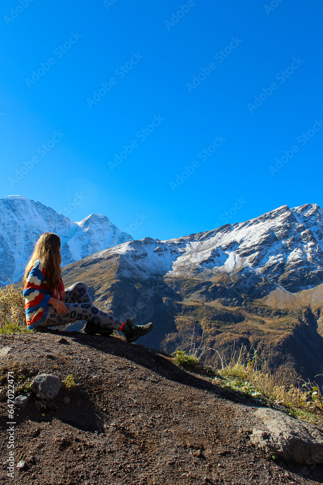 A tourist girl stands on the cliff edge of plateau against mount Elbrus, Russia A tourist girl stands on the cliff edge of plateau against mount Elbrus, Russia
