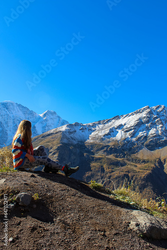 A tourist girl stands on the cliff edge of plateau against mount Elbrus, Russia