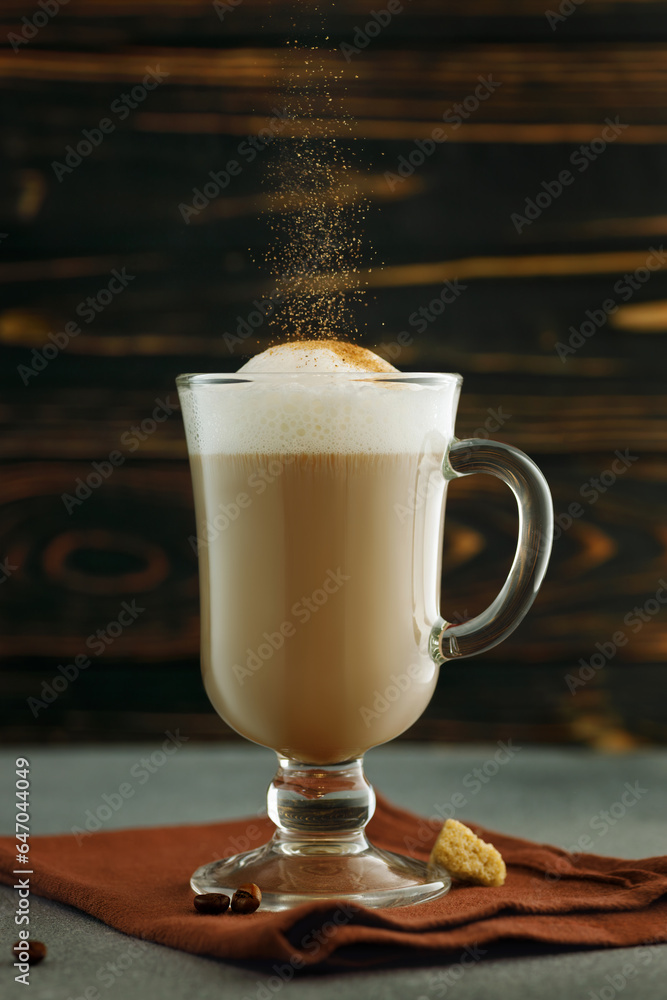 cappuccino in glass cup with falling cinnamon powder on table