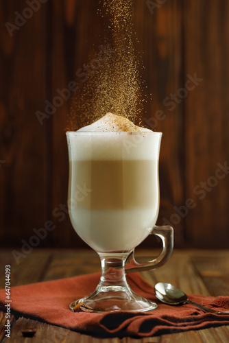 latte macchiato in glass cup with falling cinnamon powder and spoon near