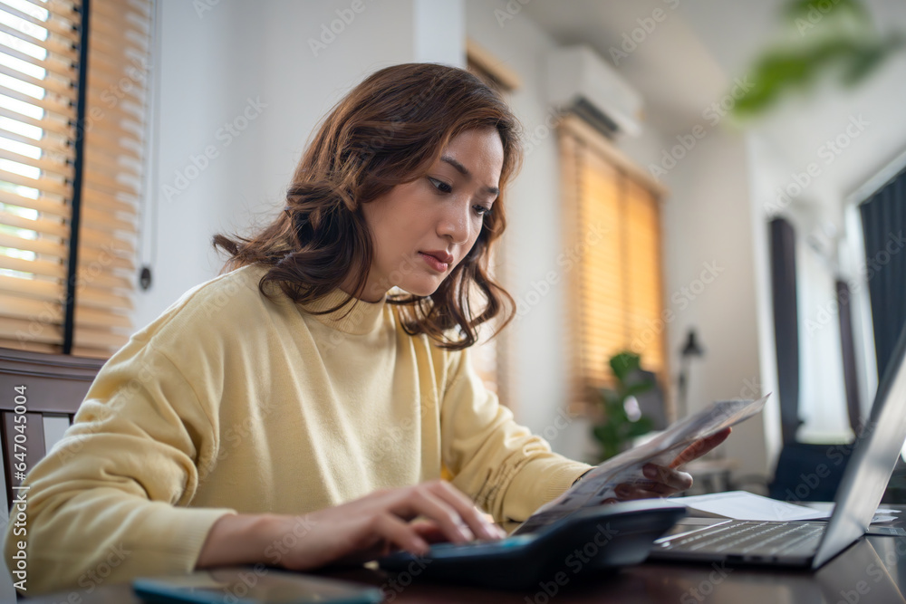 A woman uses a calculator to check the sum of her home expenses and she is stressed over the home expenses. A woman uses a calculator to check the sum of her home expenses and she is stressed over the home expenses.