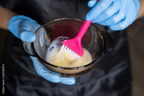 Foto girl in blue rubber protective gloves holding a brush in her hands and stirring hair dye close-up colorist hair care at home hair mask