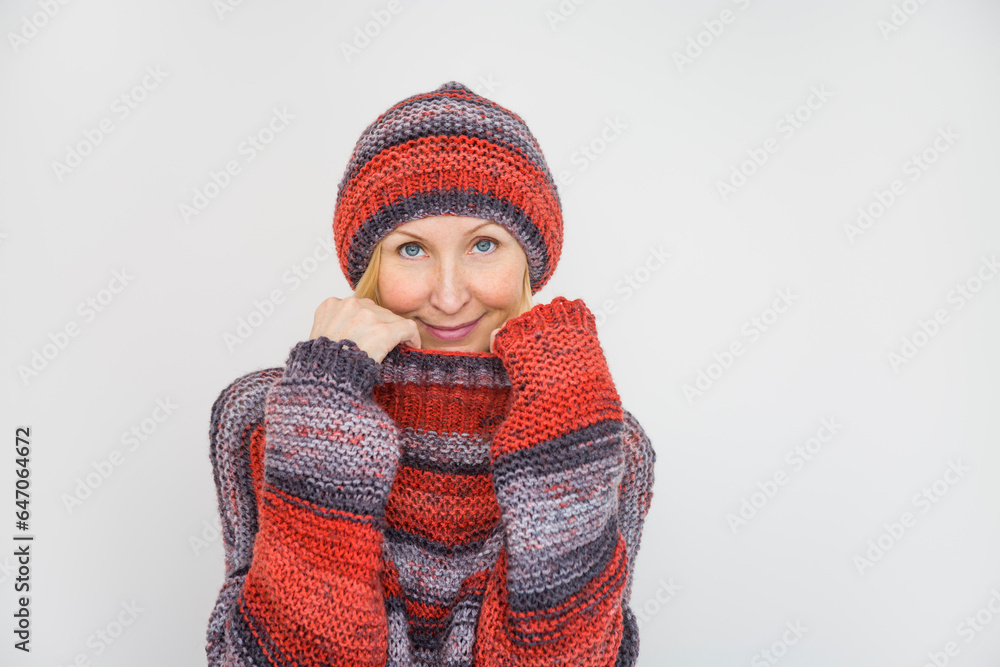 A woman dressed in a knitted terracotta sweater and a beanie pulls the collar of the sweater over her chin A woman dressed in a knitted terracotta sweater and a beanie pulls the collar of the sweater over her chin