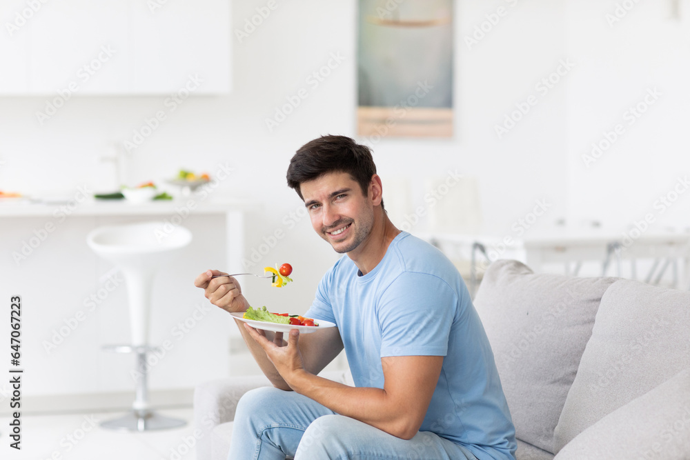 Happy man having healthy lunch with fresh salad veggies at home. Healthy food and diet concept