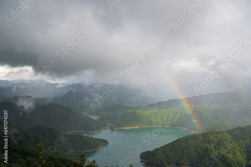 There are two rainbows in the sky by the lake. Rocky coast under blue sky and white clouds. White waves and light blue lake.