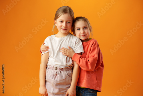 Two cute little girls standing on yellow background in the studio