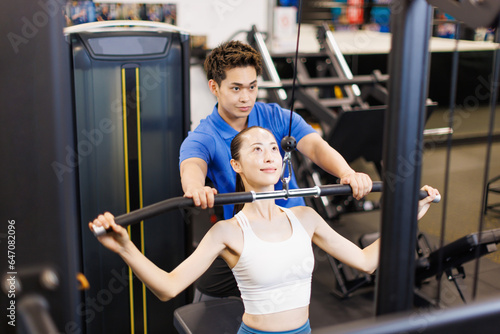 パーソナルトレーナーの指導を受けてラットプーリーで運動する若いアジアの女性