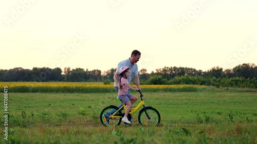 Loving father runs supporting little girl riding bicycle in summer field