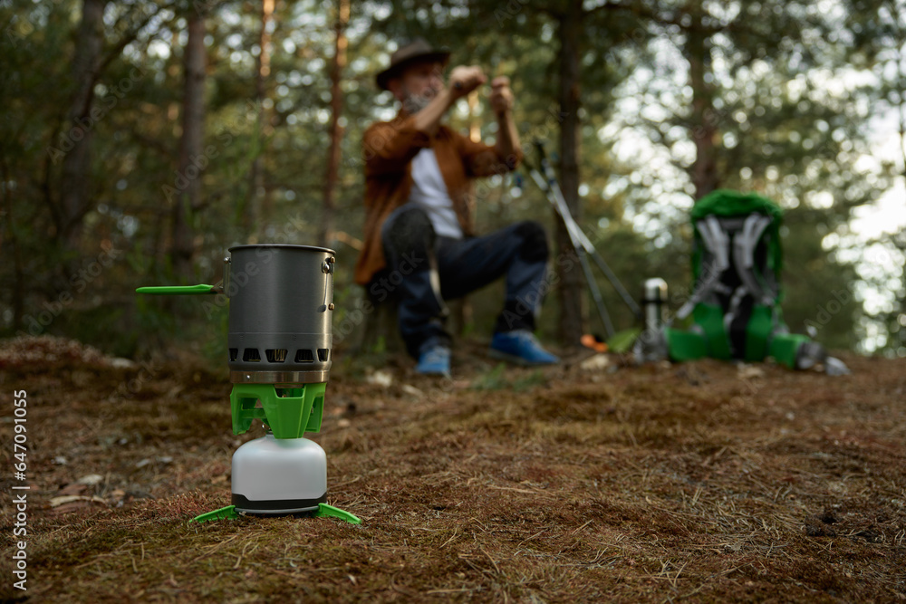 Elderly man hiker cooking food in forest, closeup view on portable gas burner Elderly man hiker cooking food in forest, closeup view on portable gas burner