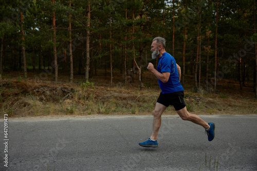 Side view motion shot of retired senior sportsman running among road