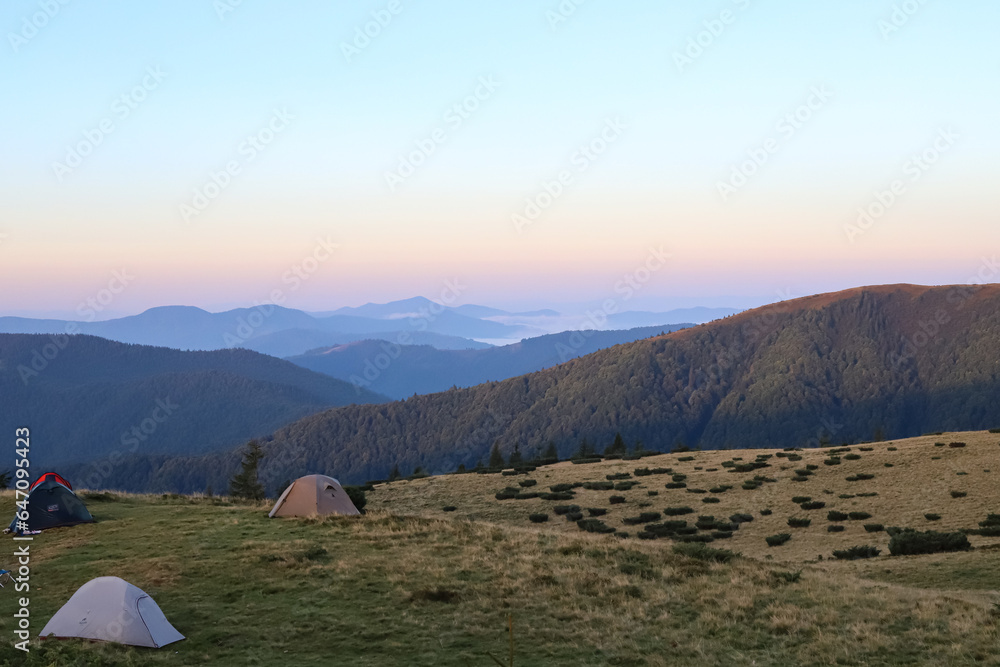 
evening in the mountains, tents stand on a mountain meadow, travel, hiking, watercolor sky after sunset in the mountains