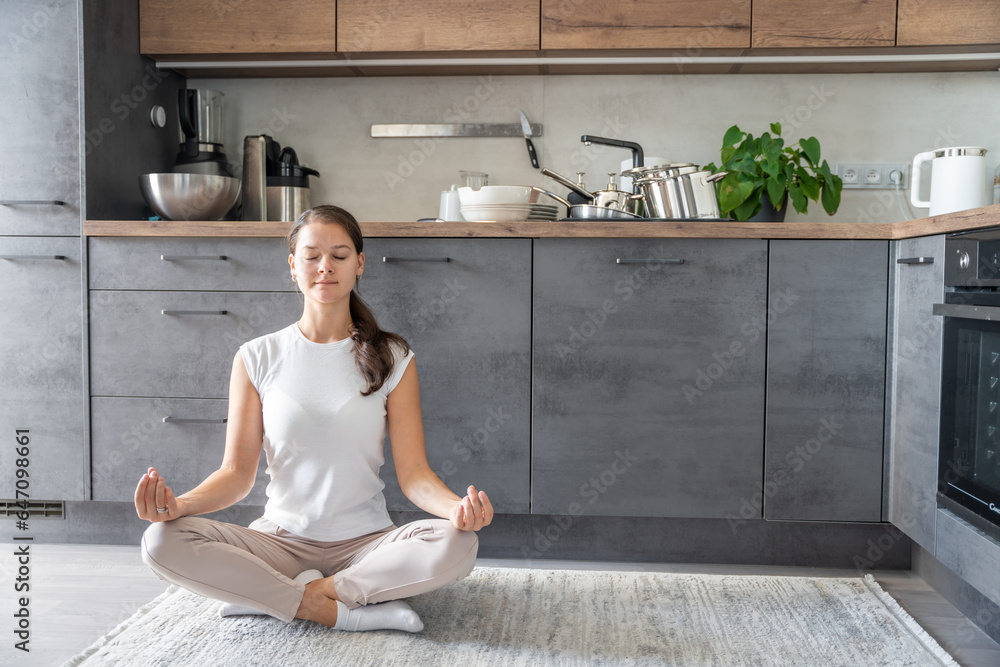 Young woman is sitting and doing meditation on background of dirty dishes in the kitchen. Slowdown, self-care, slow life concept Young woman is sitting and doing meditation on background of dirty dishes in the kitchen. Slowdown, self-care, slow life concept