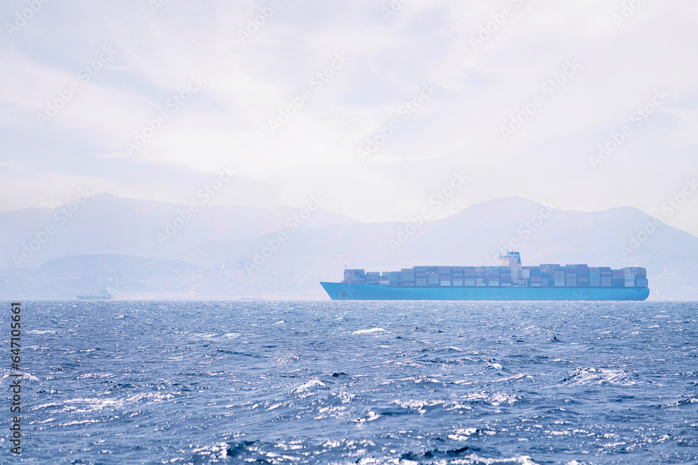 cargo ship sailing among the sea mist near the coast on a sunny day, concept of maritime transport of goods and import and export trade