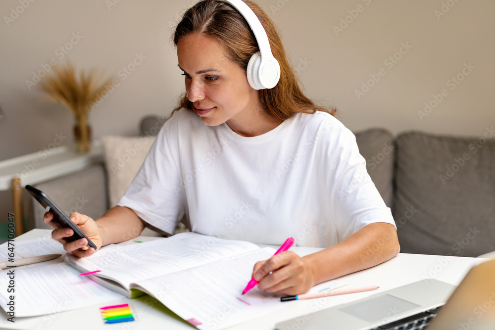 A university student is watching an educational video on the internet using her smartphone and headphones.