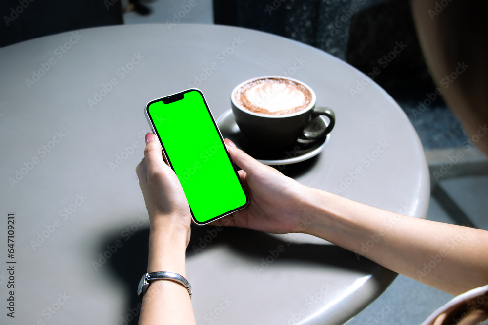 Mockup of businesswoman hand holding mobile phone with blank green screen n black table. 