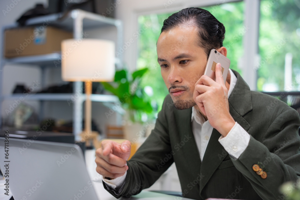 Handsome young Asia man in formal wear talking on smartphone, enjoying conversation at workplace. Young businessman using laptop in his office.
Handsome young Asia man in formal wear talking on smartphone, enjoying conversation at workplace. Young businessman using laptop in his office.