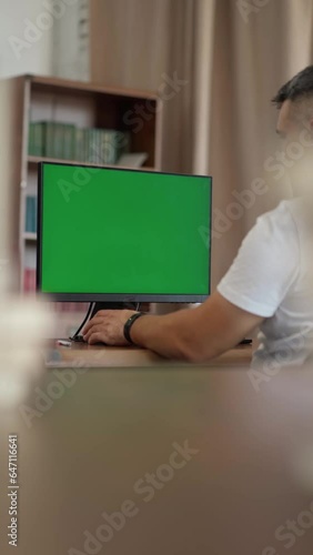 Man Working at His Desk Using Computer with Green Mock-up Screen, Chroma Key Display. Working from Cozy Home Office, Studio	