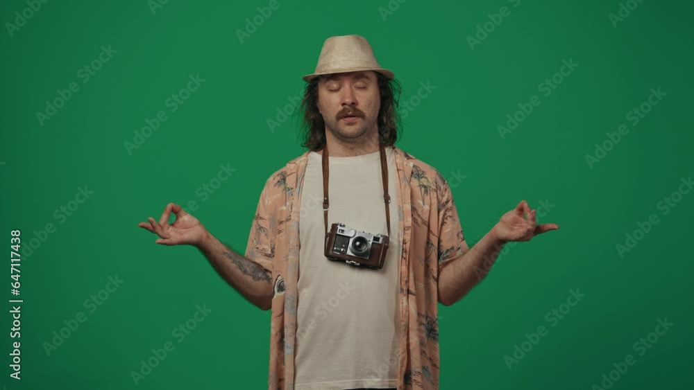Man traveller in casual clothing and straw hat wearing old film camera and holding hands in meditative position. Isolated on green background. Man traveller in casual clothing and straw hat wearing old film camera and holding hands in meditative position. Isolated on green background.