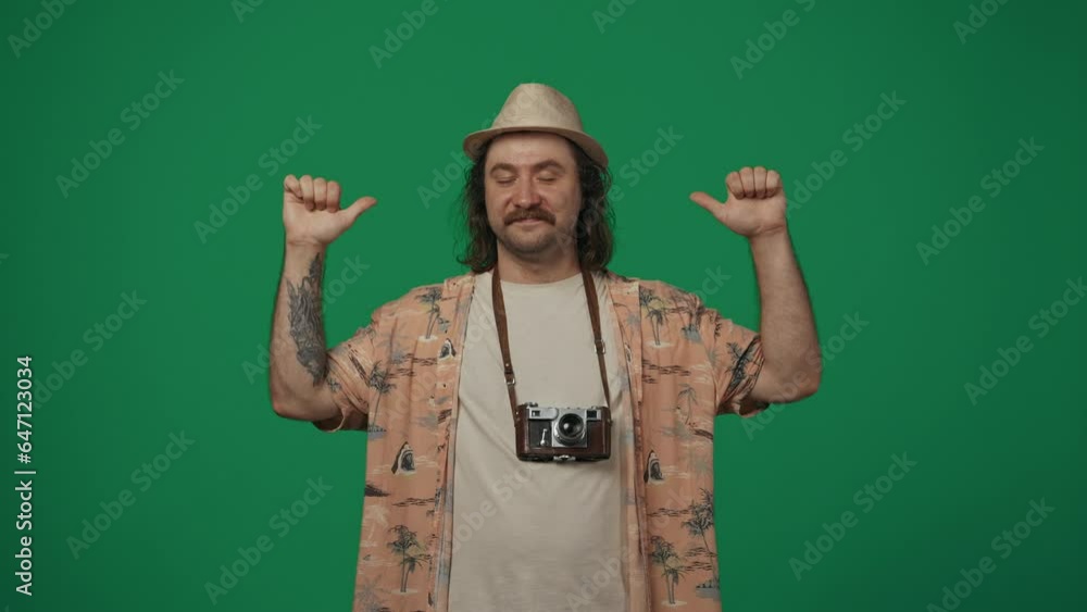Man traveller in casual clothing and straw hat with old film camera holding hands up shows thumbs up and smiles at the camera. Isolated on green background. Man traveller in casual clothing and straw hat with old film camera holding hands up shows thumbs up and smiles at the camera. Isolated on green background.
