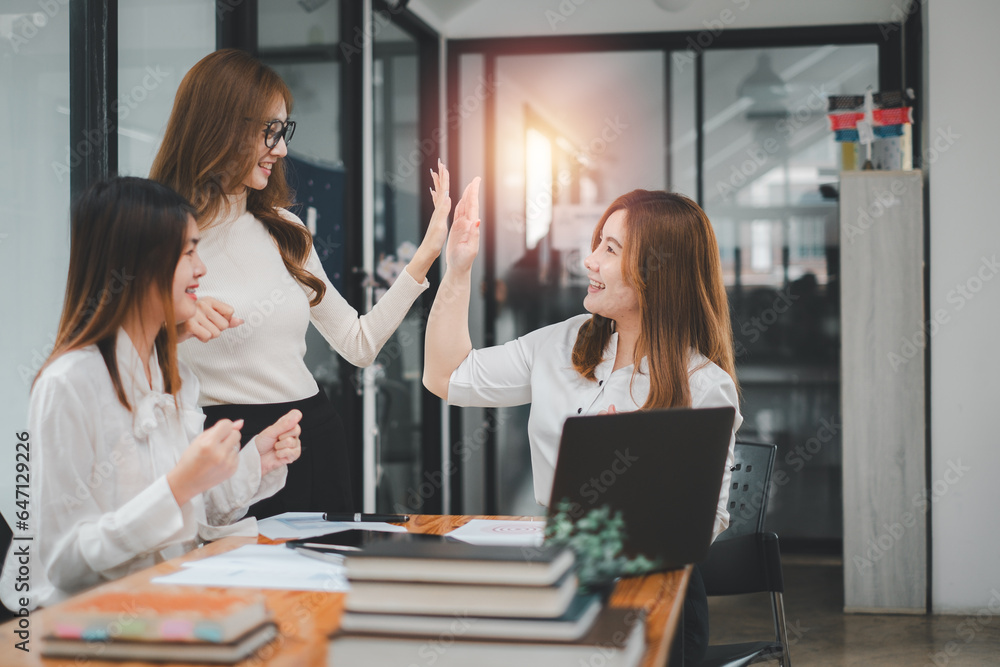 Business team giving a high five to female colleague in meeting. Business professionals high five during a meeting in boardroom. Business team giving a high five to female colleague in meeting. Business professionals high five during a meeting in boardroom.