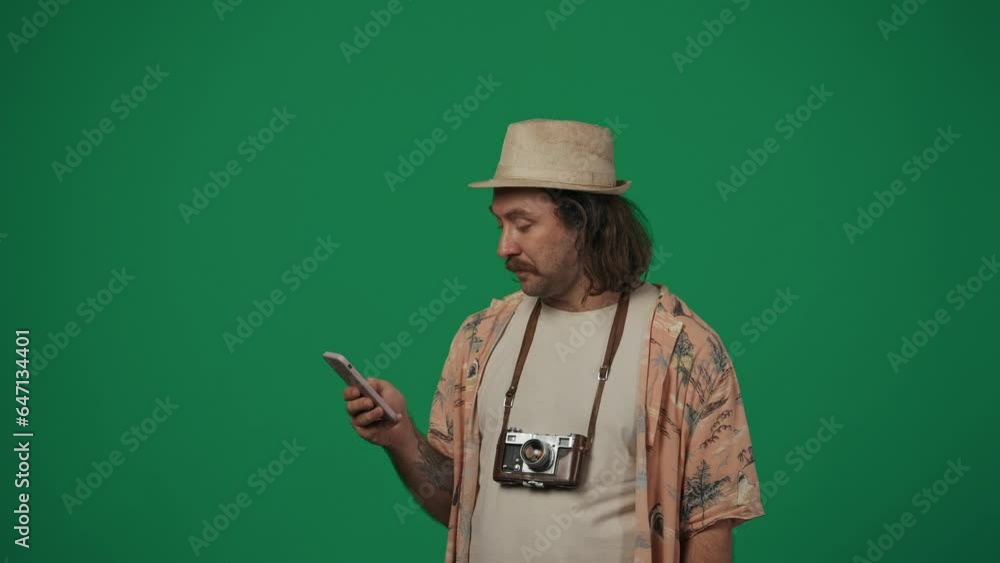 Man in casual clothing and straw hat with old film camera found something on smartphone, holding money bills, shouting with amazed face. Isolated on green background. Man in casual clothing and straw hat with old film camera found something on smartphone, holding money bills, shouting with amazed face. Isolated on green background.
