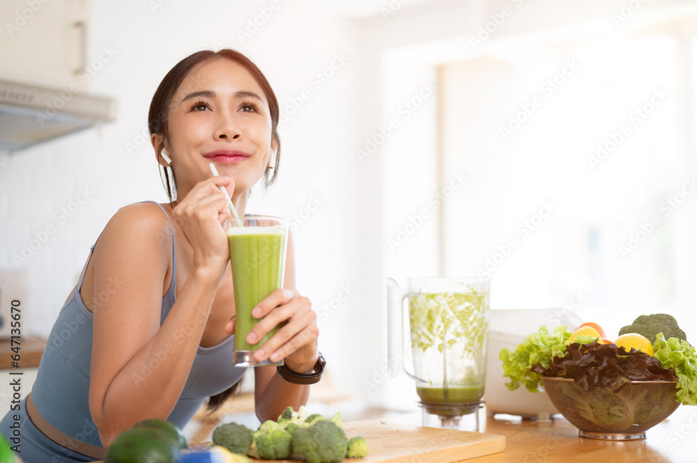 A beautiful Asian woman is enjoying her healthy green smoothie in the kitchen after her workout. A beautiful Asian woman is enjoying her healthy green smoothie in the kitchen after her workout.