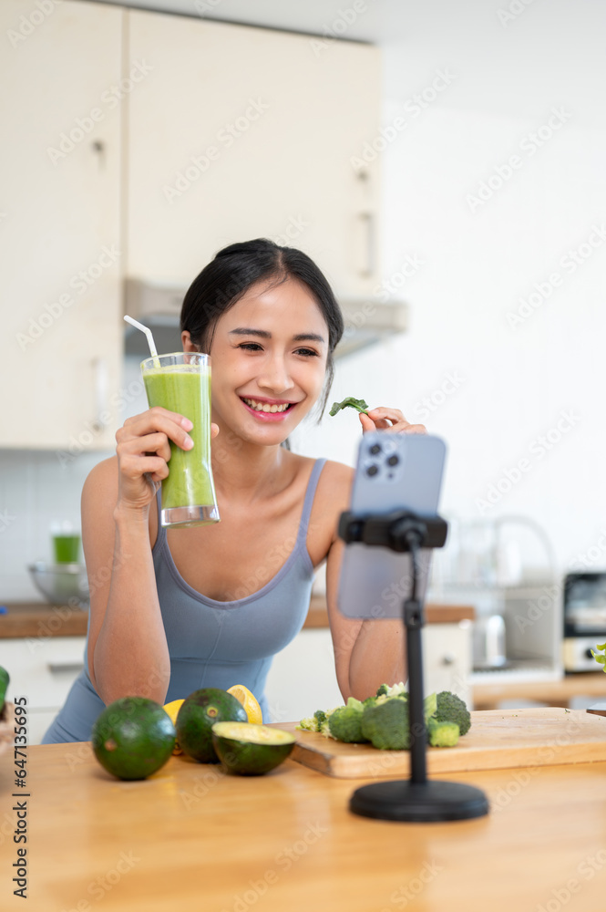 An attractive Asian female influencer is live streaming online while making her healthy smoothie.